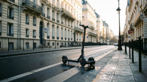 Scooters électriques stationnés près d’une piste cyclable dans une rue parisienne, avec des immeubles historiques en arrière-plan.